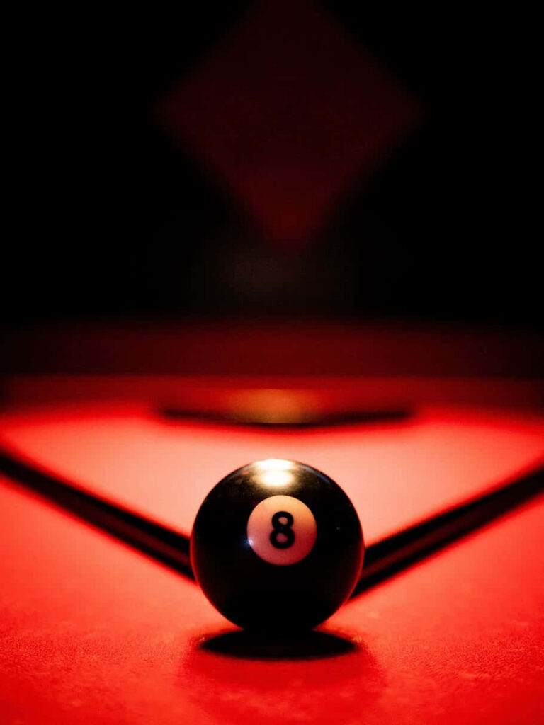 Close-up of black eight-ball on vibrant red pool table with dramatic lighting and shadows wallpaper