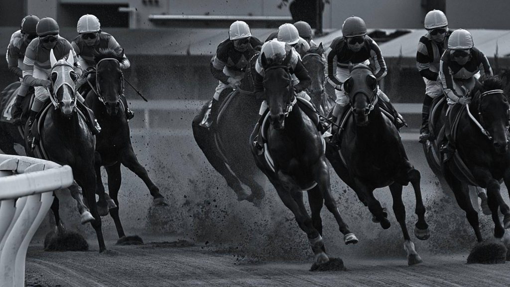 Black and white horse racing wallpaper showing jockeys racing fast on dirt track in action shot