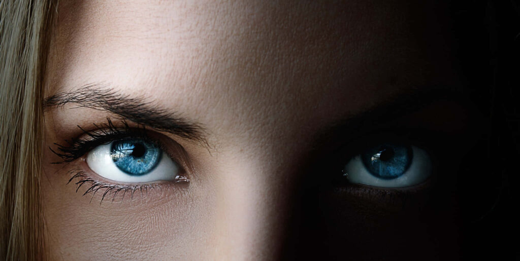 Closeup of woman with vivid blue eyes dramatic lighting sharp gaze realistic wallpaper background