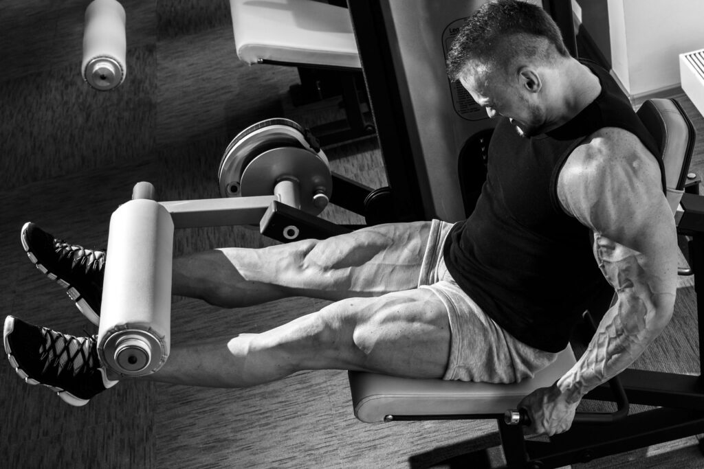 Bodybuilder performing leg extension exercise showing muscle strength in black and white wallpaper