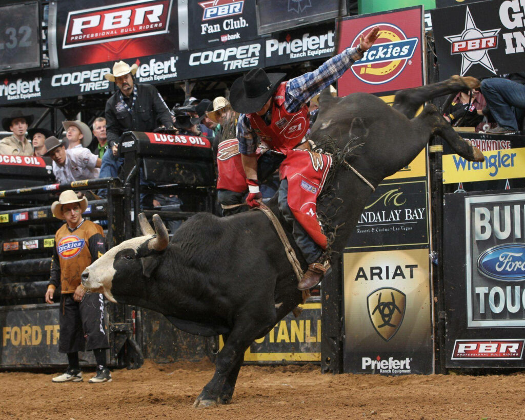 Pro bull rider grips bucking bull in lively rodeo arena with dust and rugged cowboy style wallpaper