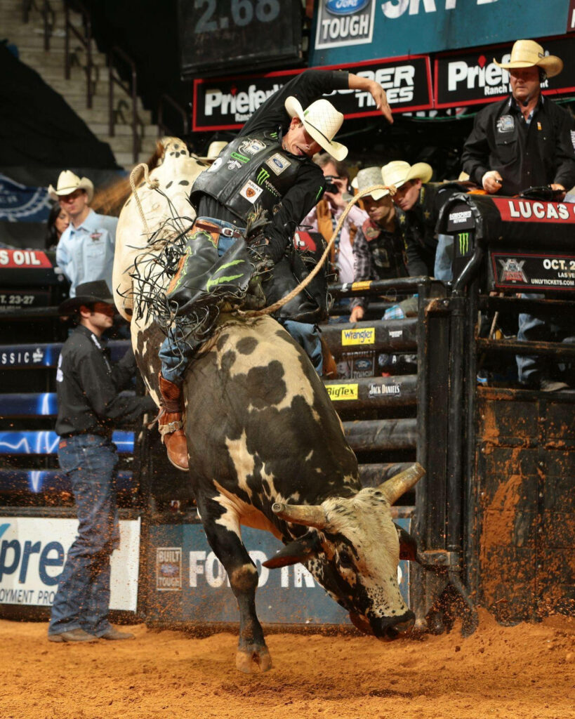 Cowboy riding powerful bull in vibrant rodeo arena with intense Western action and energy Wallpaper