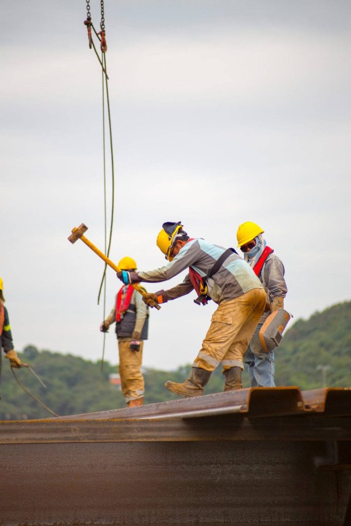 Construction workers in yellow hard hats swinging sledgehammer on outdoor industrial site wallpaper