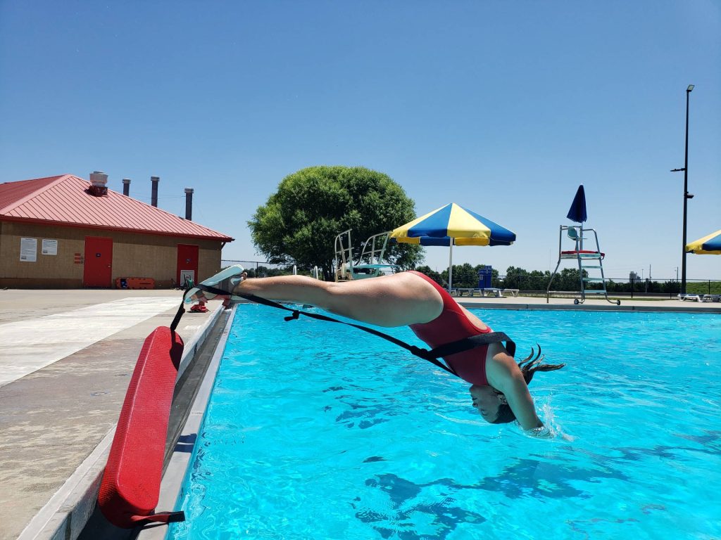 Lifeguard in red swimsuit diving into blue pool during intense summer rescue drill training session Wallpaper