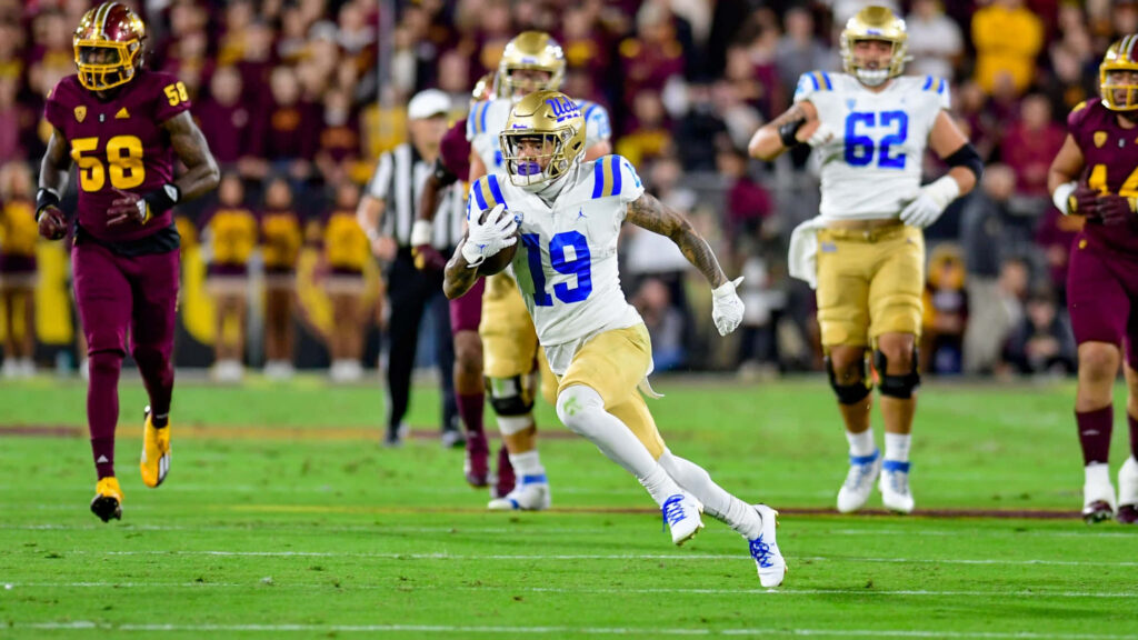 Football player in white and blue uniform sprinting with ball in intense game under stadium lights Wallpaper