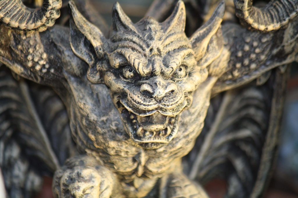 Close-up of a weathered gothic stone gargoyle with sharp horns and menacing expression outdoors Wallpaper