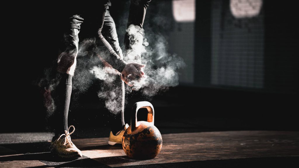 Faceless athlete claps chalk dust over worn kettlebell in intense gym workout photo background Wallpaper