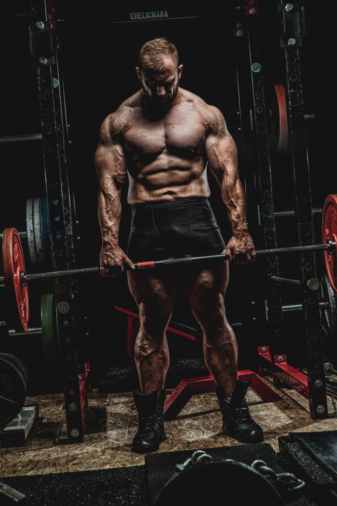 Muscular bodybuilder gripping barbell in dark power rack intense gym motivation wallpaper background