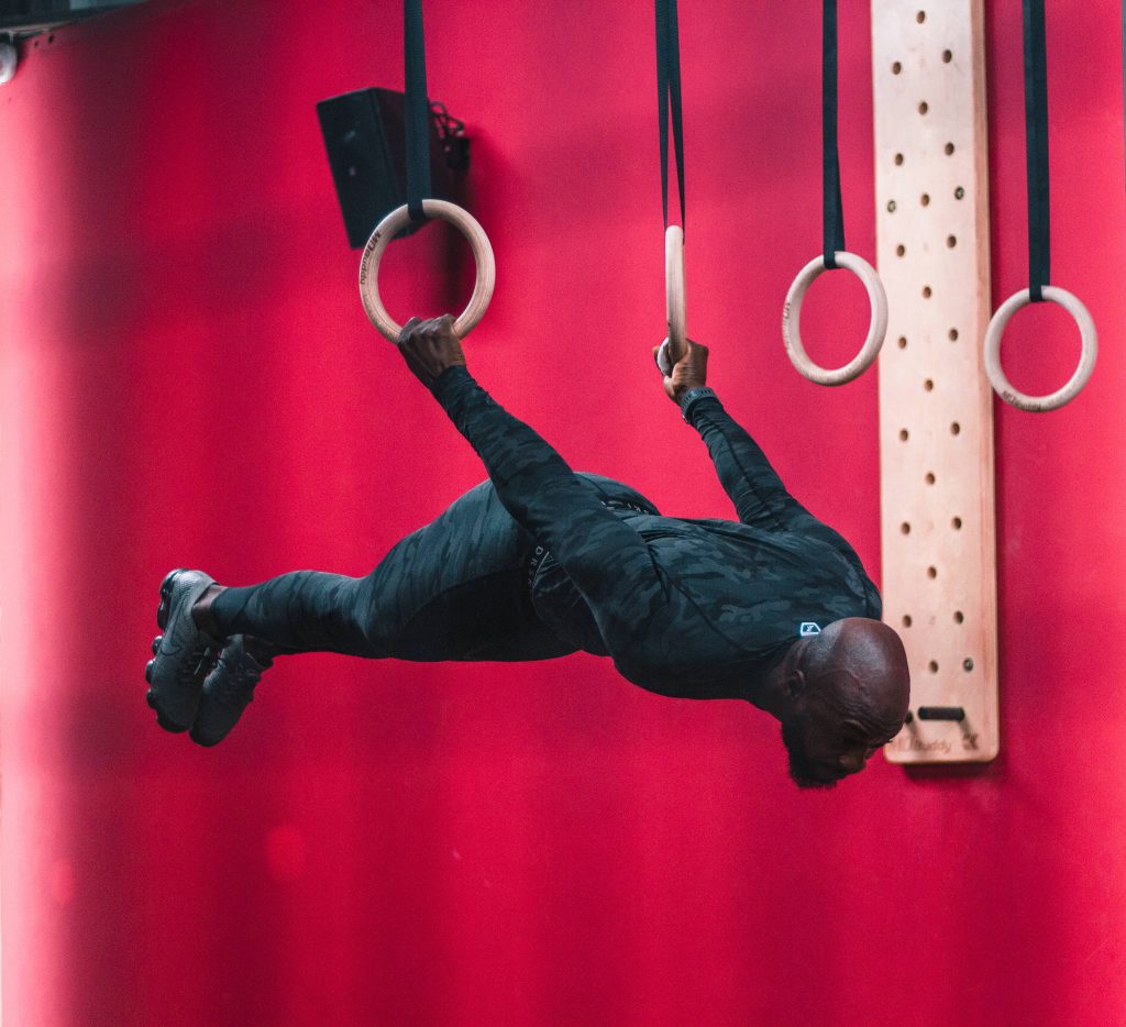 Athlete in camo activewear holds back lever on wooden rings red wall fitness wallpaper background