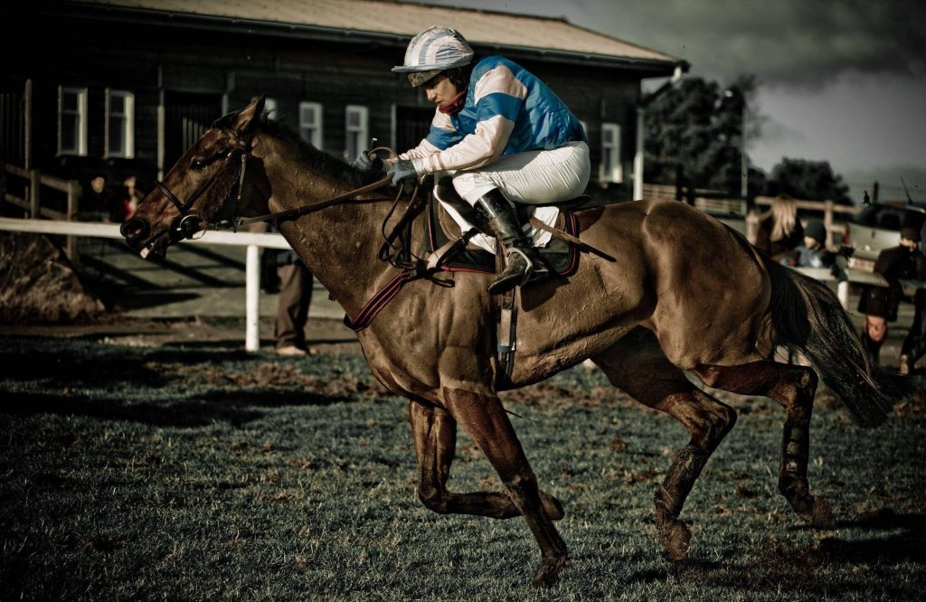 Thoroughbred horse and jockey racing on muddy track under moody overcast sky wallpaper background
