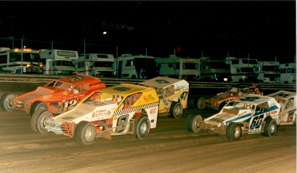 Night dirt track racing with colorful modified cars kicking up dust under stadium lights Wallpaper