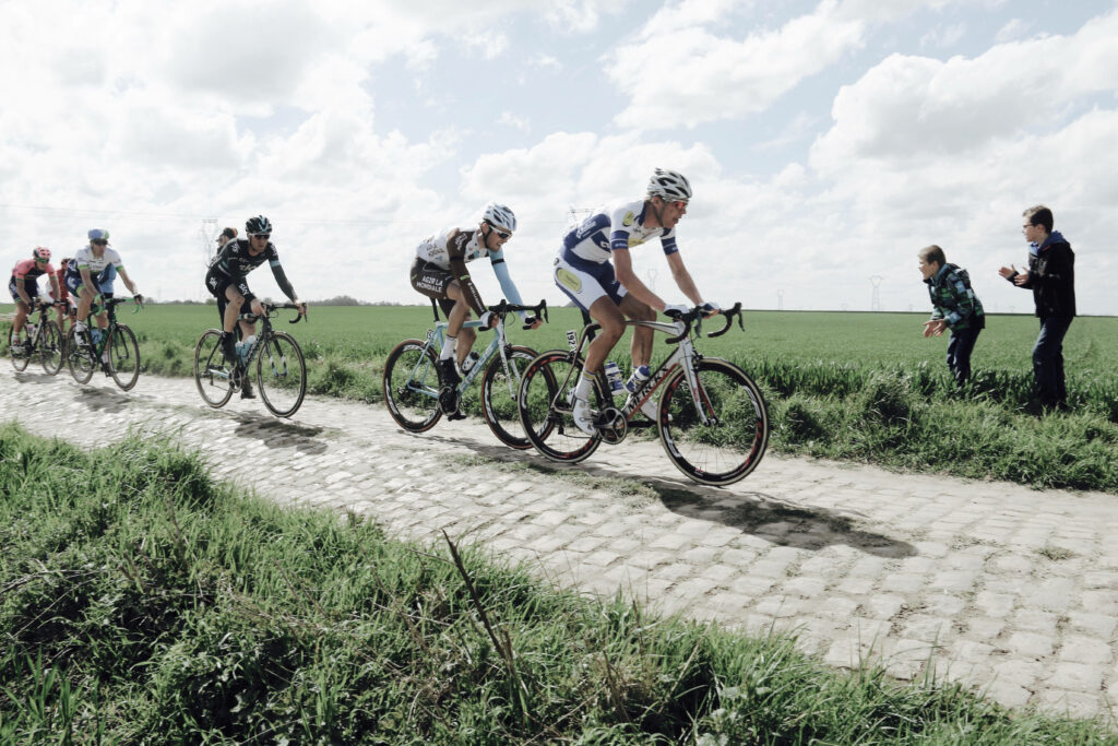 Men cycling intensely on rustic cobblestone path surrounded by green fields on sunny day wallpaper