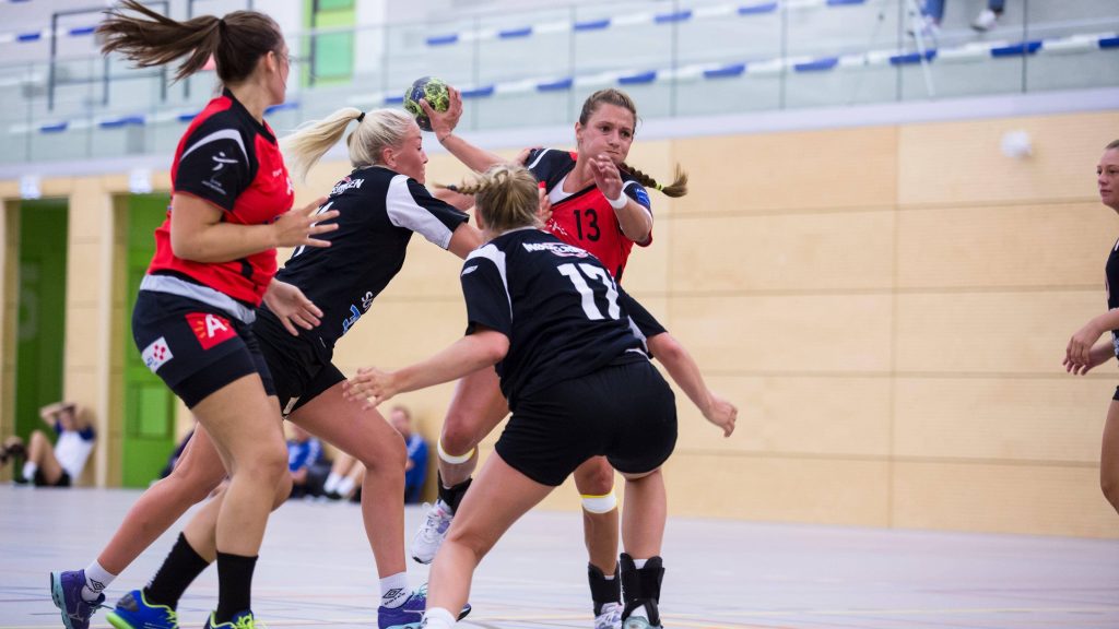 Professional women's handball players in red and black uniforms in dynamic mid-action game Wallpaper