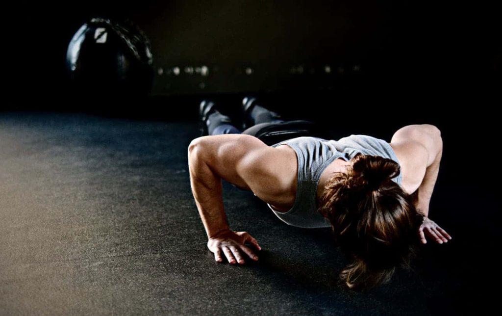 Person doing push-up in dim gym with dramatic lighting showcasing muscle definition fitness wallpaper