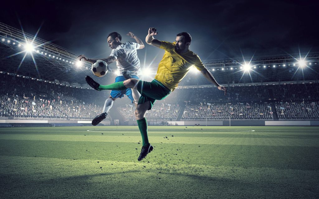 Two soccer players compete mid-air under stadium floodlights on a vibrant night football pitch Wallpaper