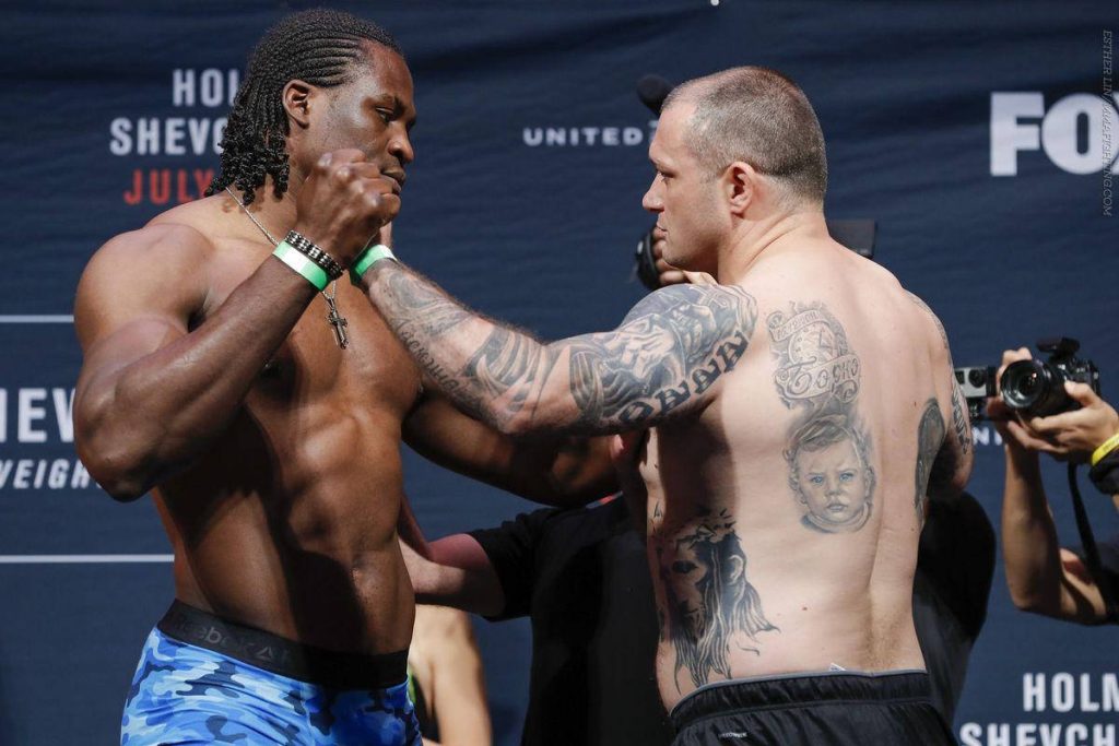 Two muscular UFC fighters in intense faceoff at weigh-in with branded dark blue backdrop Wallpaper