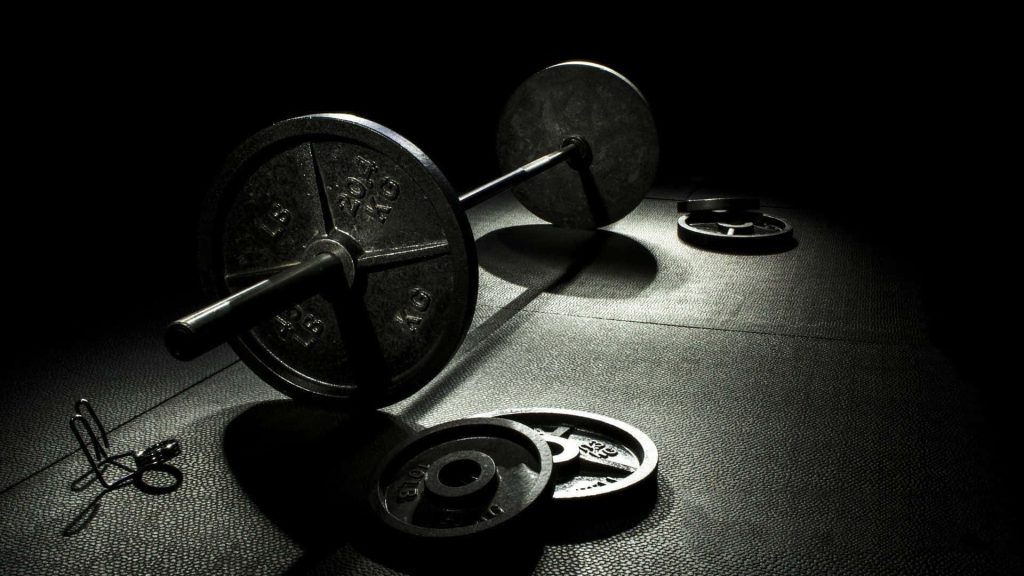 Loaded barbell on textured gym floor with dramatic lighting intense weight training wallpaper