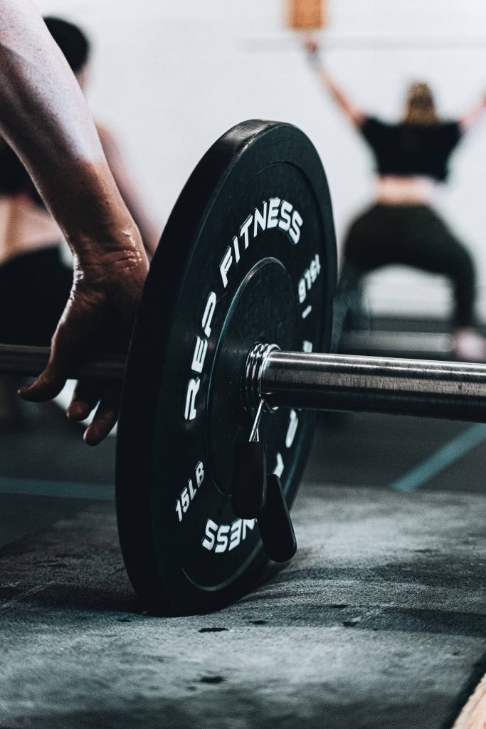 Close-up of hand gripping Rep Fitness barbell plate in moody gym weightlifting wallpaper background