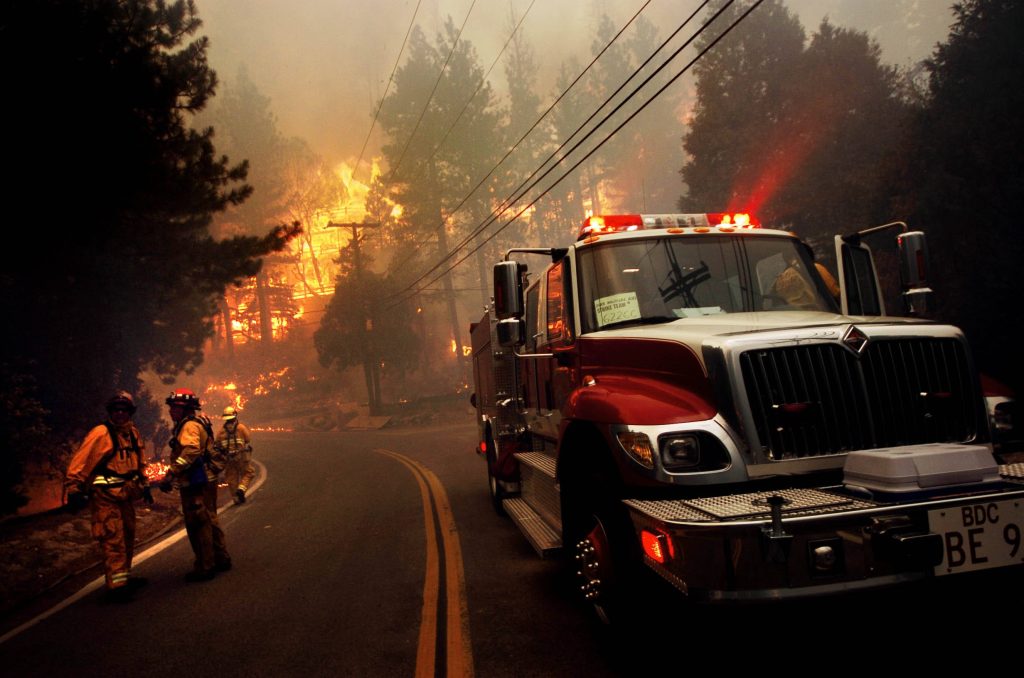 Firefighters in full gear beside red fire engine battling intense wildfire with flames and smoke Wallpaper