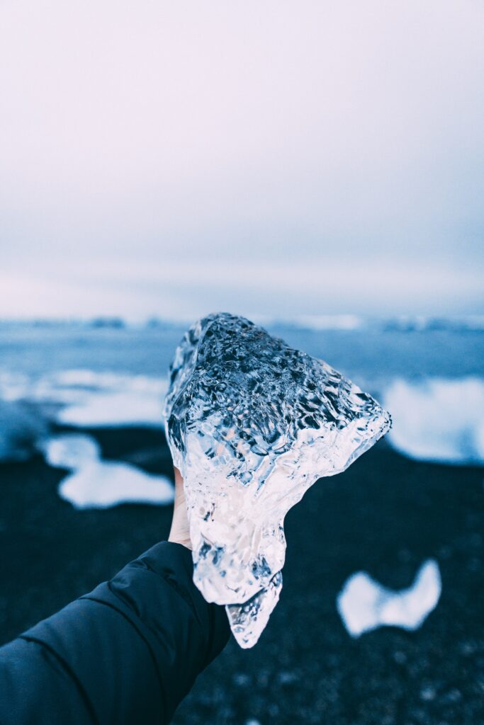 Gloved hand holding clear patterned ice chunk with icy floes and cold blue winter landscape background Wallpaper