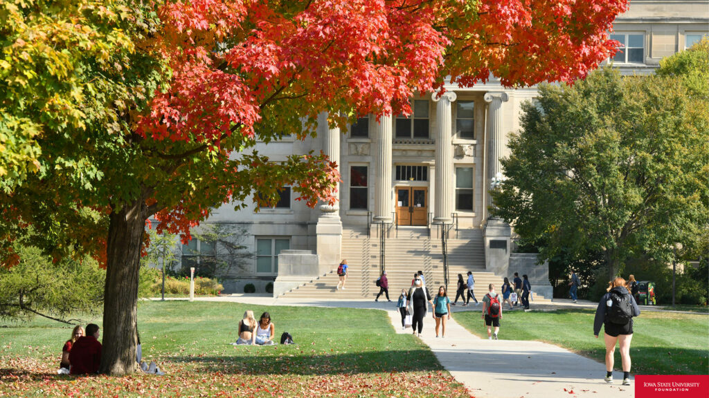 Iowa State University campus lawn with students autumn foliage and historic building in daylight Wallpaper
