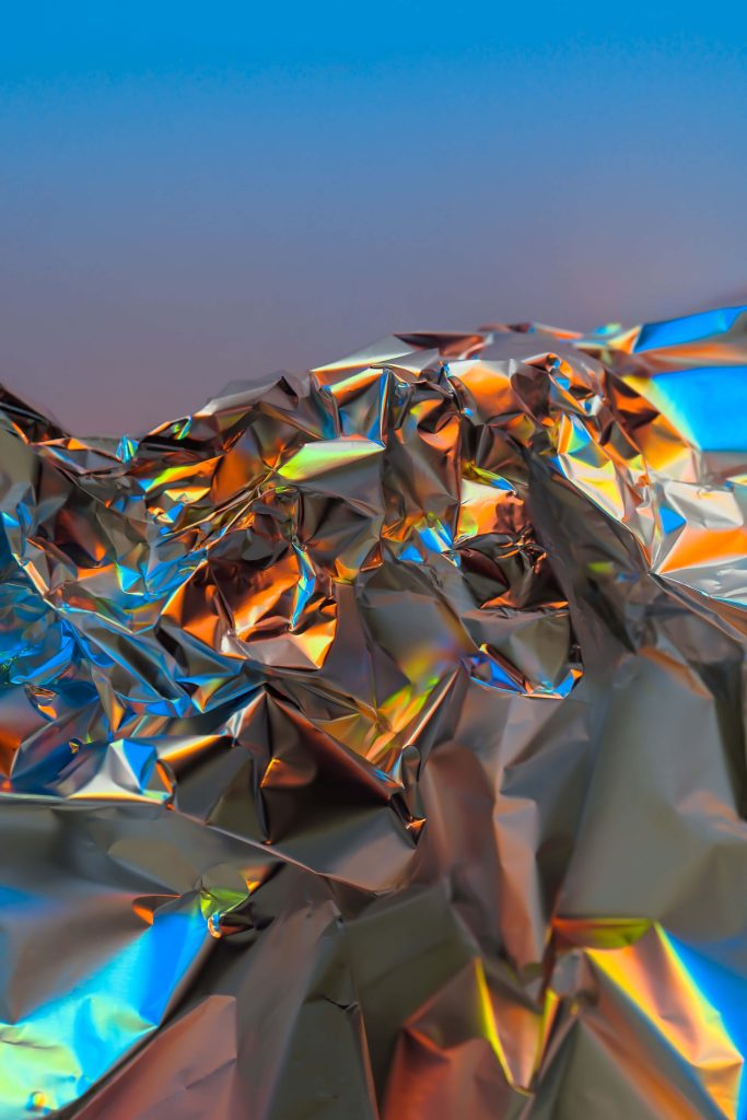 Abstract crumpled iridescent foil wallpaper with vibrant holographic orange and blue reflections