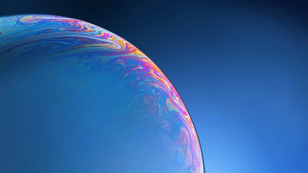 Macro iridescent soap bubble surface with swirling colors on deep blue minimalist wallpaper