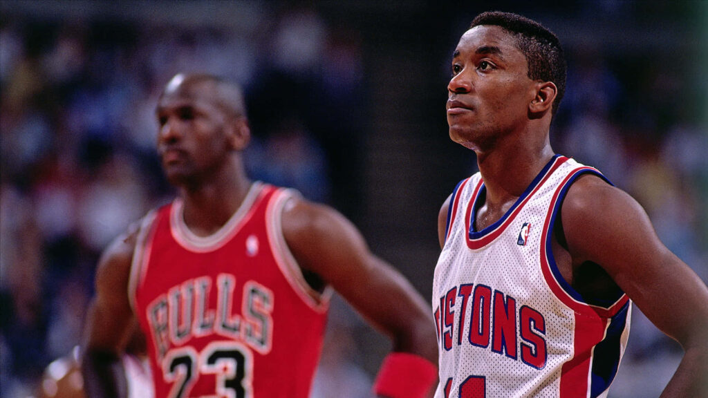 Isiah Thomas in Detroit Pistons jersey sharp with blurred Michael Jordan Chicago Bulls background wallpaper