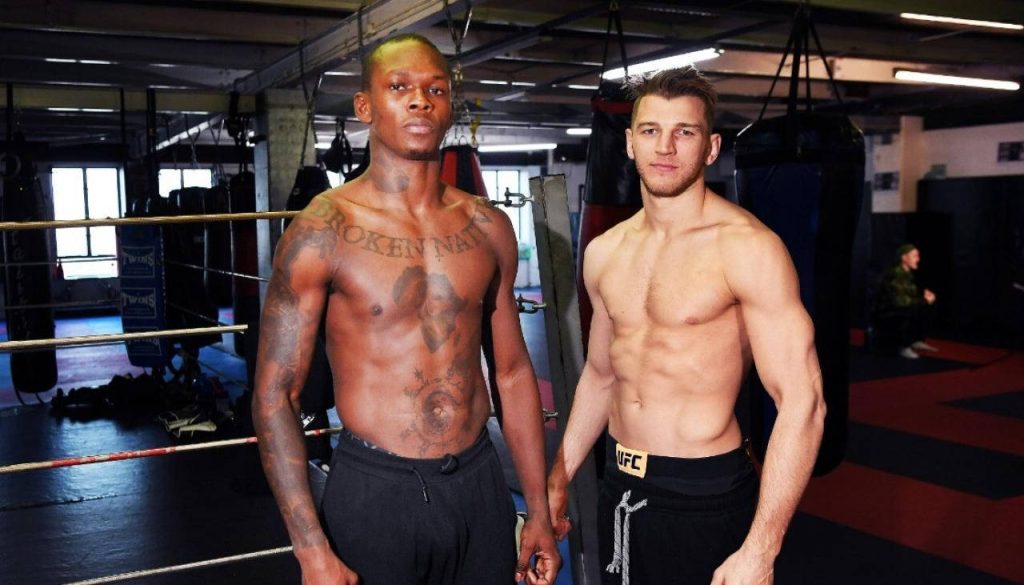 UFC fighters Israel Adesanya and Dan Hooker shirtless in gym with boxing ring ropes and heavy bags Wallpaper