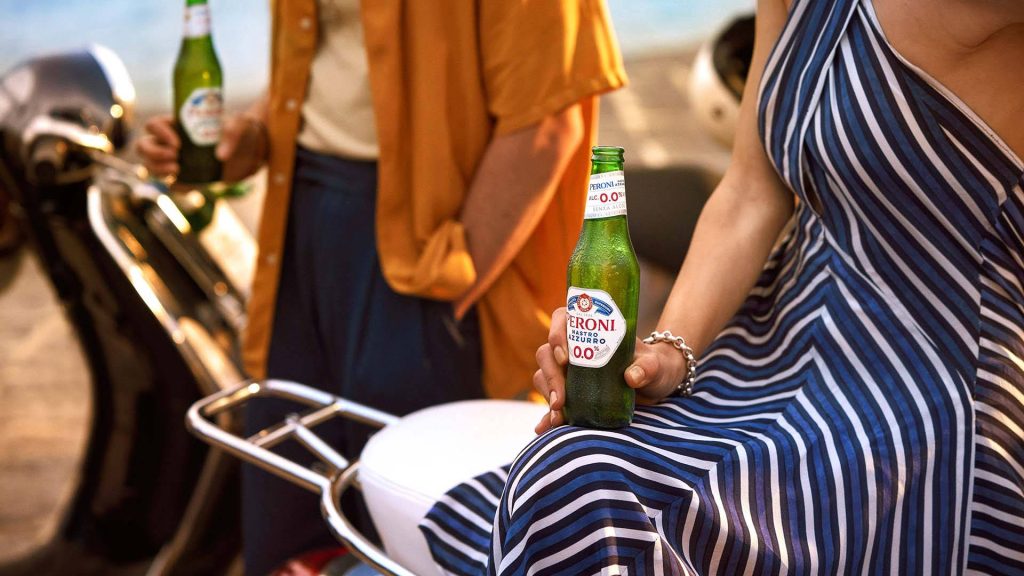 Stylish woman with Peroni Nastro Azzurro 00 beer and classic scooter in sunny Italian summer Wallpaper