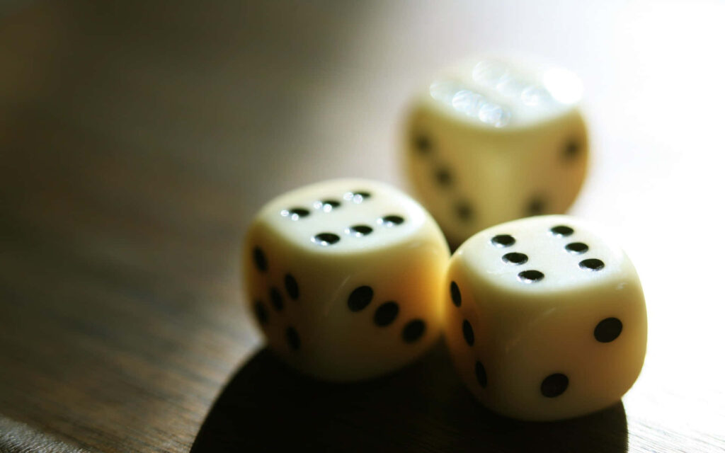 Three ivory dice with black dots on wooden surface soft light casting gentle shadows gaming wallpaper