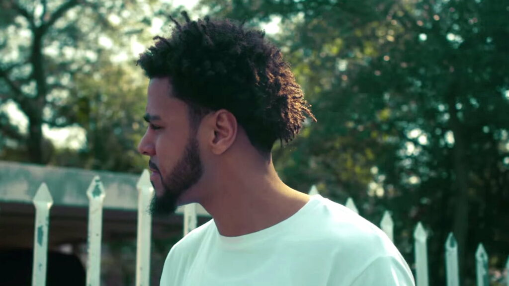 J Cole's Serene Stance: Vibrant Green Ambience Embracing the Essence of Music Wallpaper
