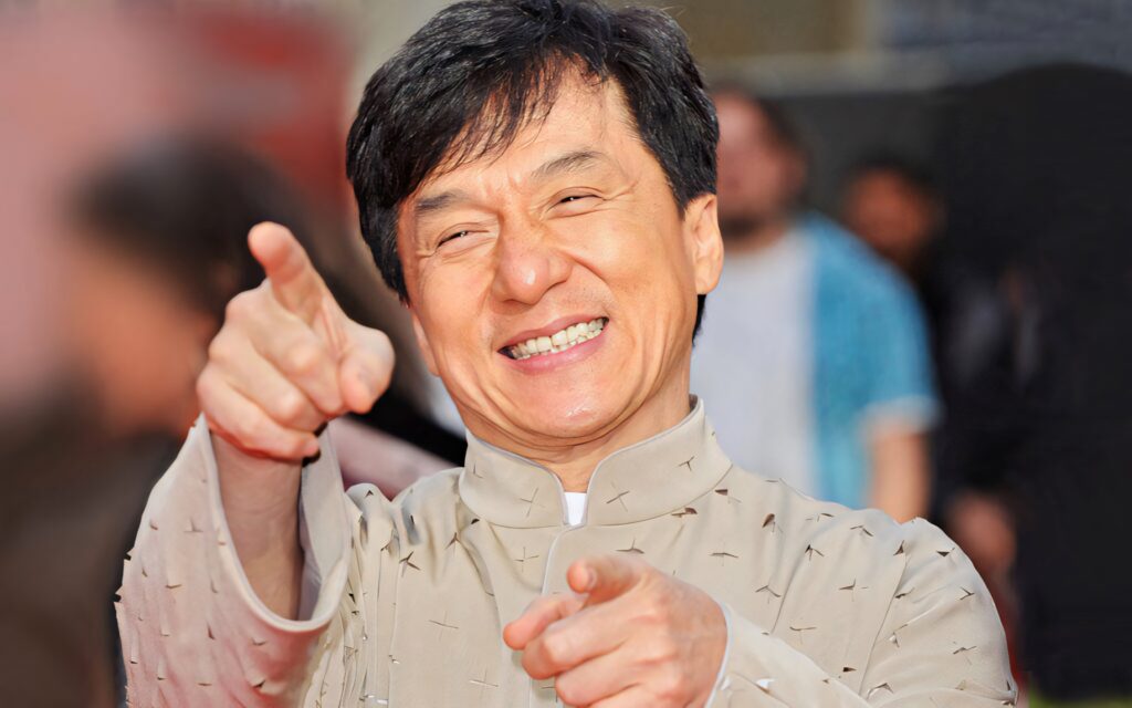 Jackie Chan laughing and playfully pointing at camera energetic wallpaper background image