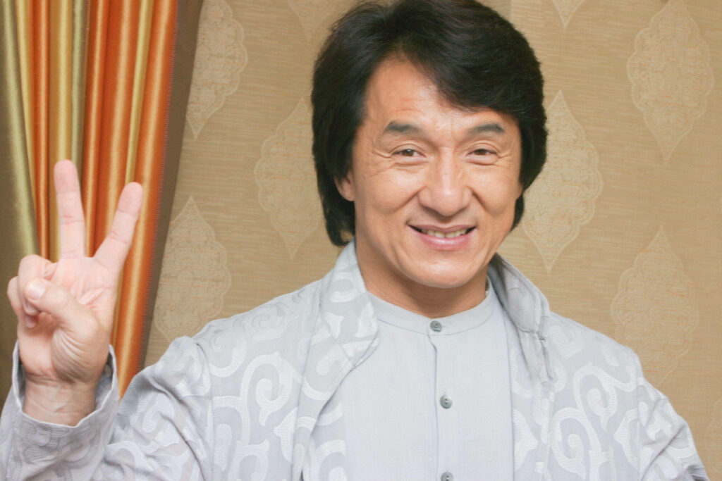 Jackie Chan smiling warmly making peace sign cheerful wallpaper background image