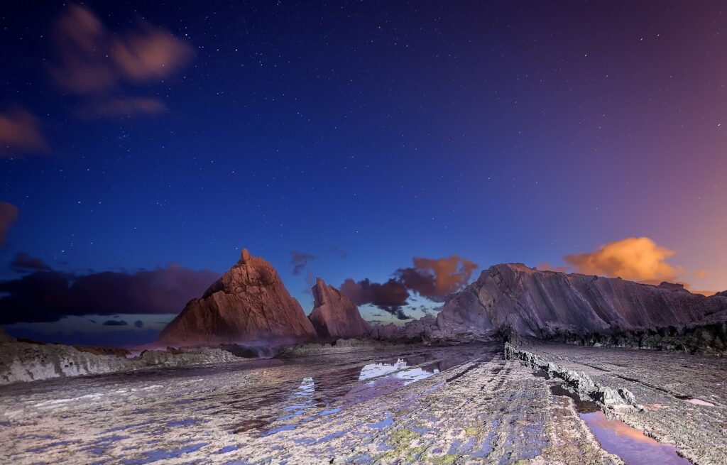 Jagged mountains at dusk with purple blue sky stars wispy clouds and reflective rocky terrain wallpaper