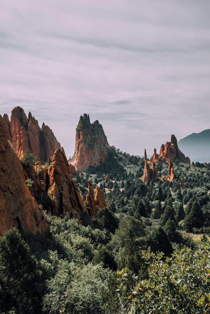 Jagged red rock formations above green trees and shrubs under a soft cloudy sky landscape wallpaper