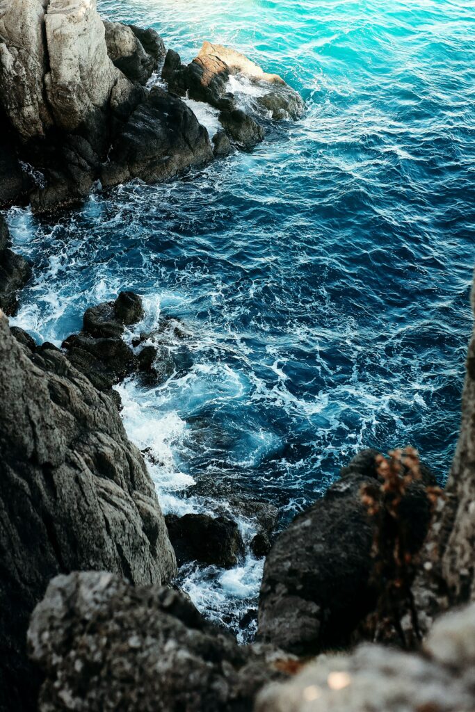 Jagged rocks and turquoise waves crash along rugged coastline creating vibrant coastal wallpaper
