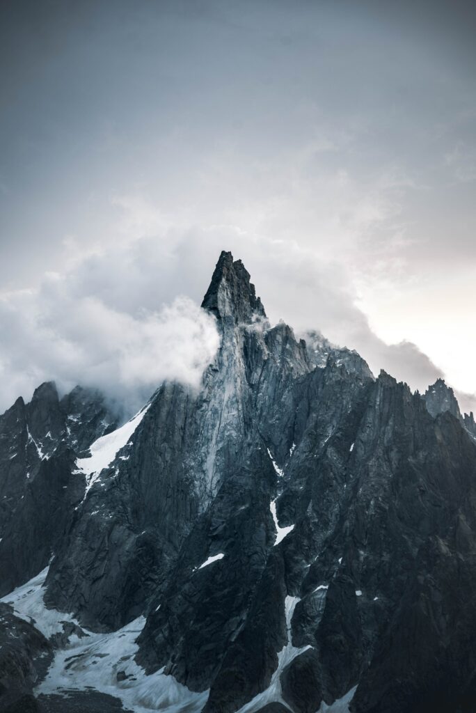 Jagged rocky peak piercing swirling clouds with snow patches dramatic mountain wallpaper background