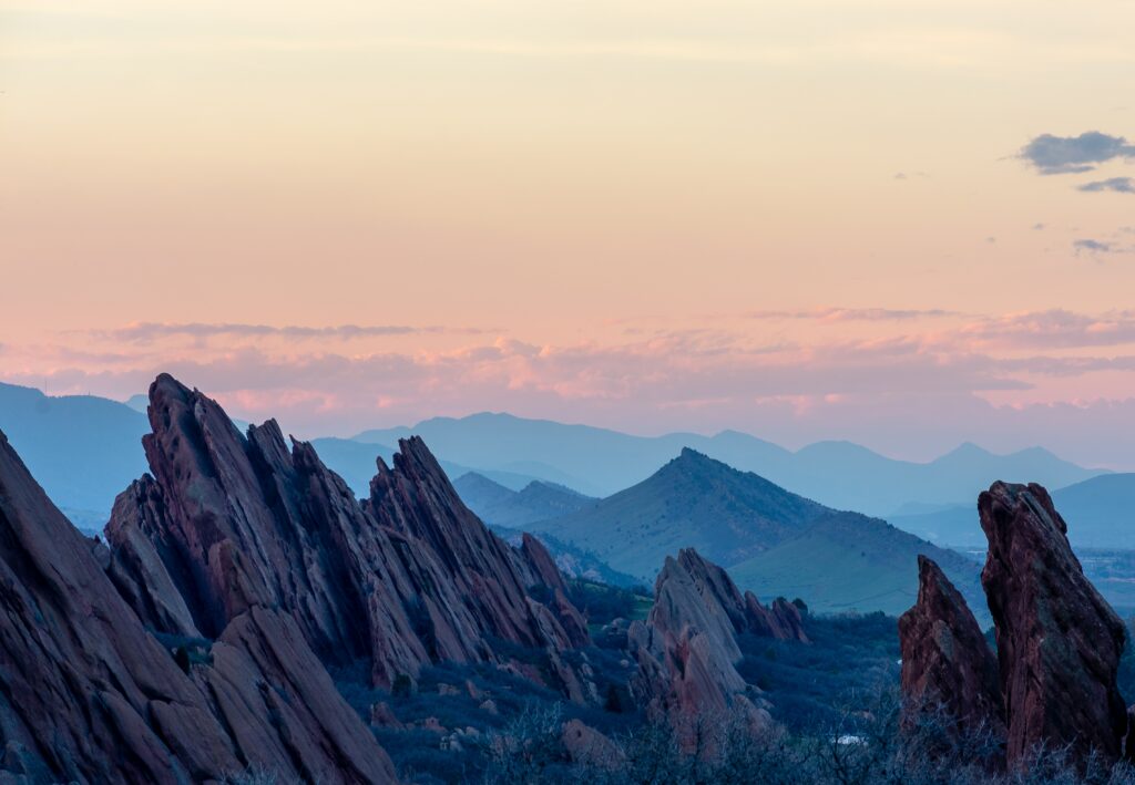 Jagged stone formations and serene pastel mountains at sunset natural landscape wallpaper background