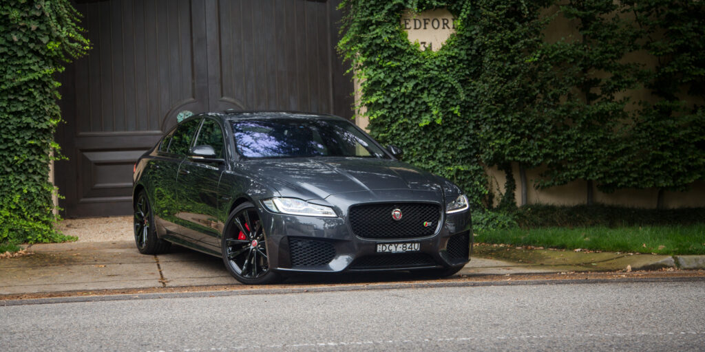 Sleek Jaguar XF: Elegant Side View Against Lush Green Background Wallpaper
