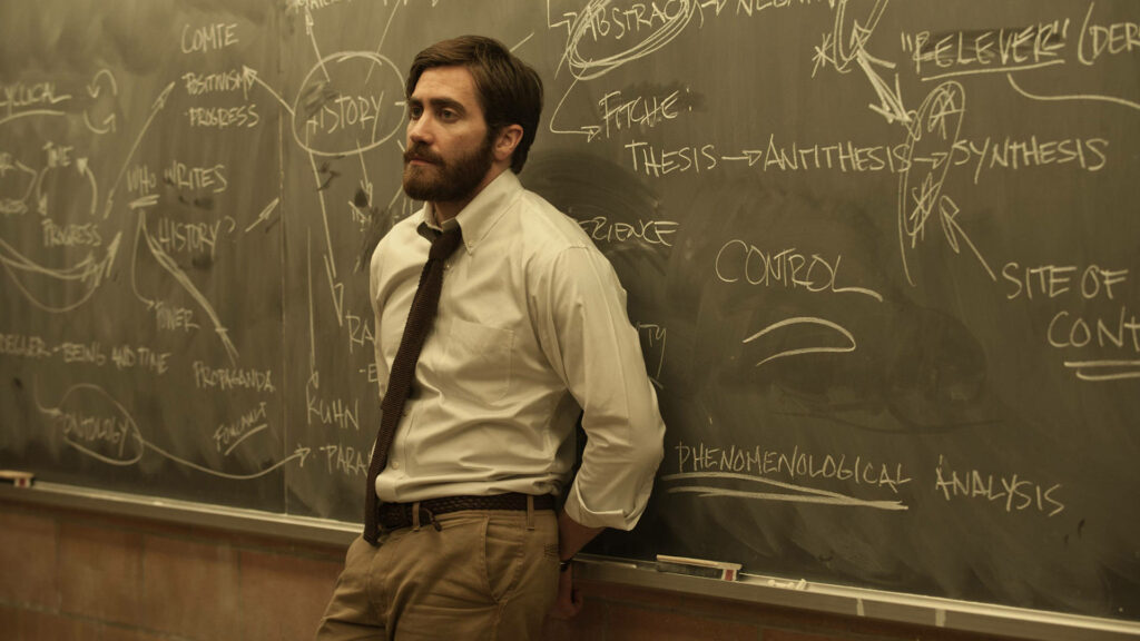 Jake Gyllenhaal leans on blackboard with complex notes and diagrams scholarly wallpaper background