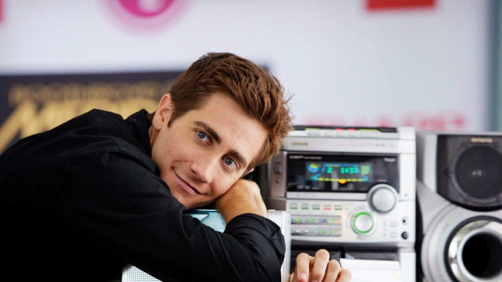 Jake Gyllenhaal leaning against stereo smiling warmly charming wallpaper background image