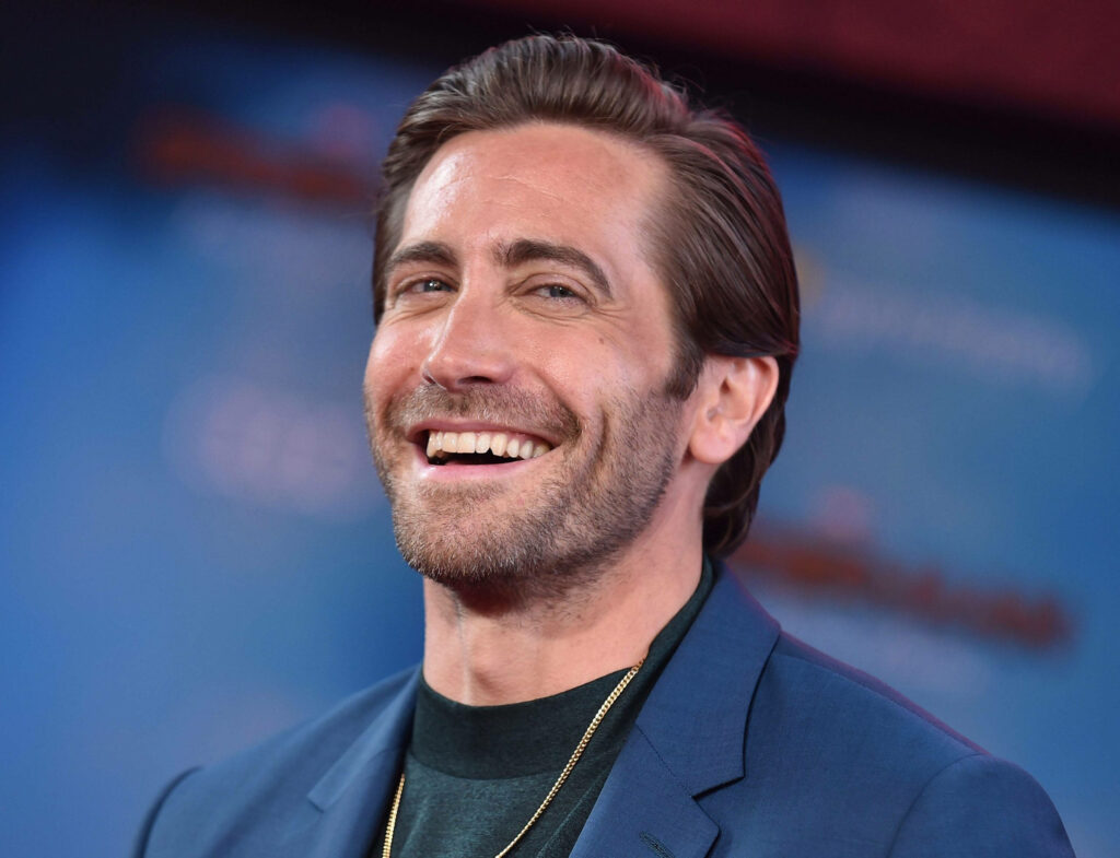 Jake Gyllenhaal smiling in sharp blue suit vibrant blurred blue background wallpaper image