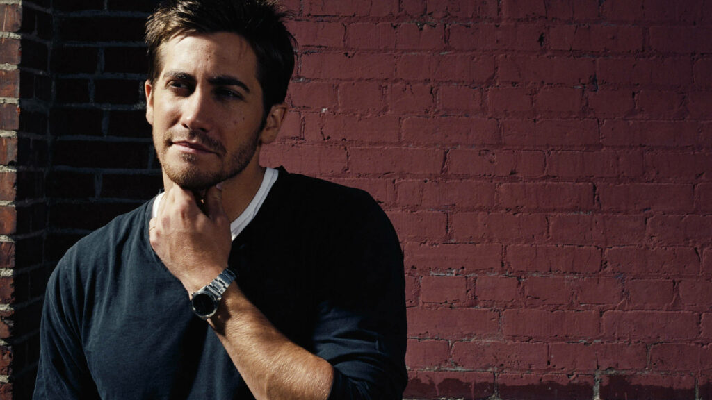 Jake Gyllenhaal confident pose against rustic red brick wall Hollywood actor wallpaper background