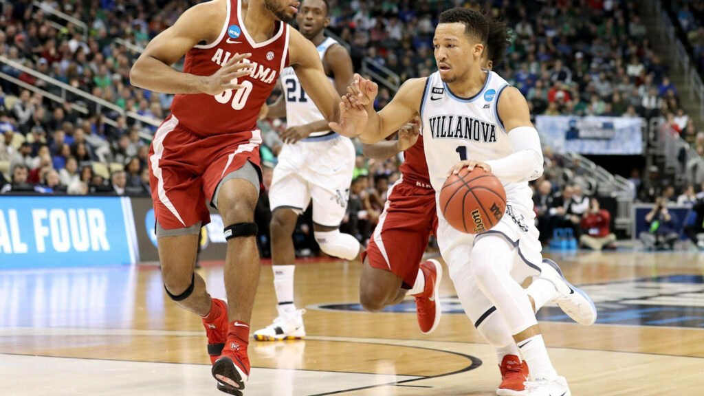 Jalen Brunson dribbling past defenders in Villanova uniform during intense basketball game action Wallpaper