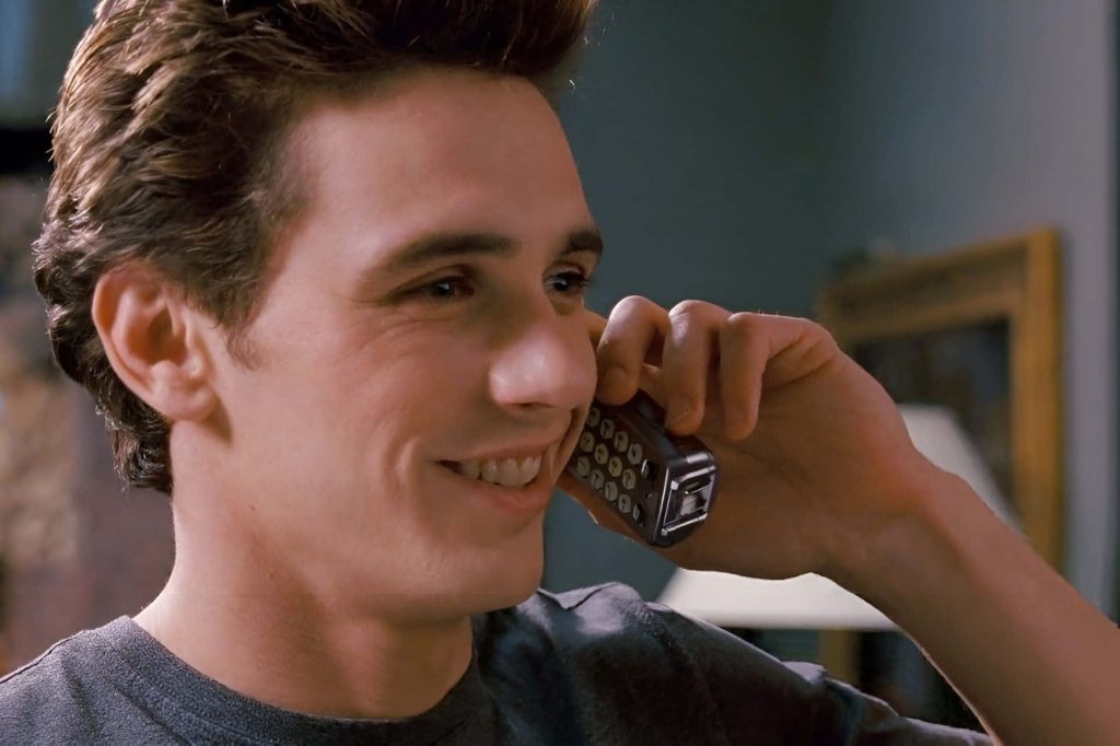 James Franco as Harry Osborn smiling with retro flip phone in Spider-Man movie scene wallpaper