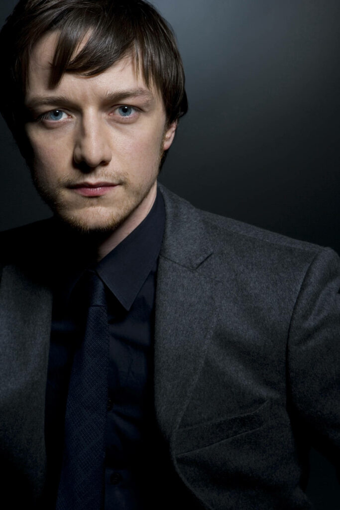 Close-up portrait of James McAvoy in dark suit with intense gaze on subdued wallpaper background