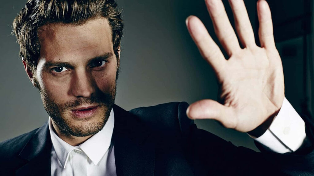 Jamie Dornan portrait in suit with serious expression hand raised dramatic captivating wallpaper