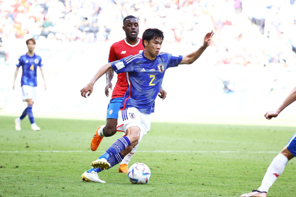 Japan defender Yamane in blue jersey in action against Costa Rica on sunlit green football pitch Wallpaper