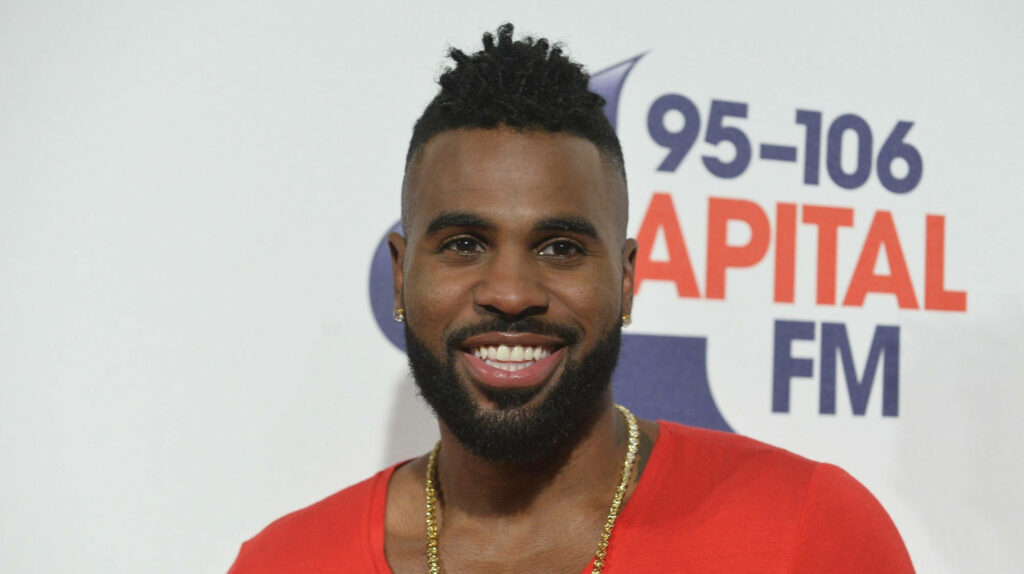 Jason Derulo smiling in red shirt and gold chain at Capital FM backdrop wallpaper background
